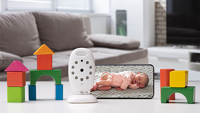 Sur une table, des structures faites en blocs, un babyphone de la marque Kindekraft et un smartphone avec l'image en direct d'un bébé qui dort. 