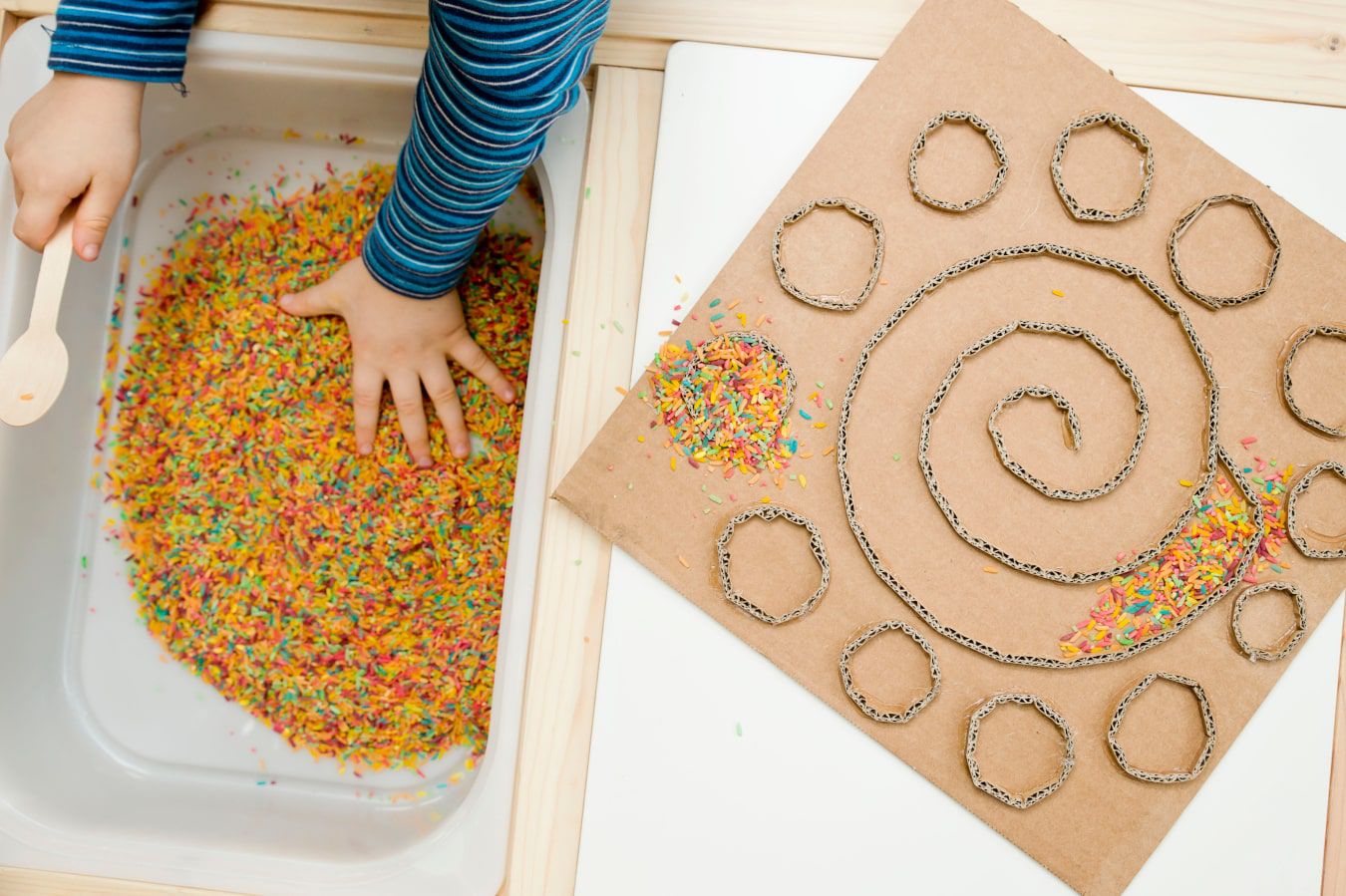 Les mains de bébé reconnaissent une nouvelle texture - des bonbons colorés et des vermicelles, à côté il y a un labyrinthe en carton DIY