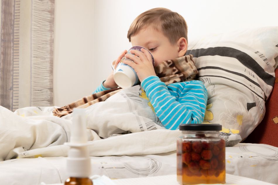 Un garçon malade boit du thé chaud dans une tasse. Sur la table, il y a un sirop de framboise contre le rhume.